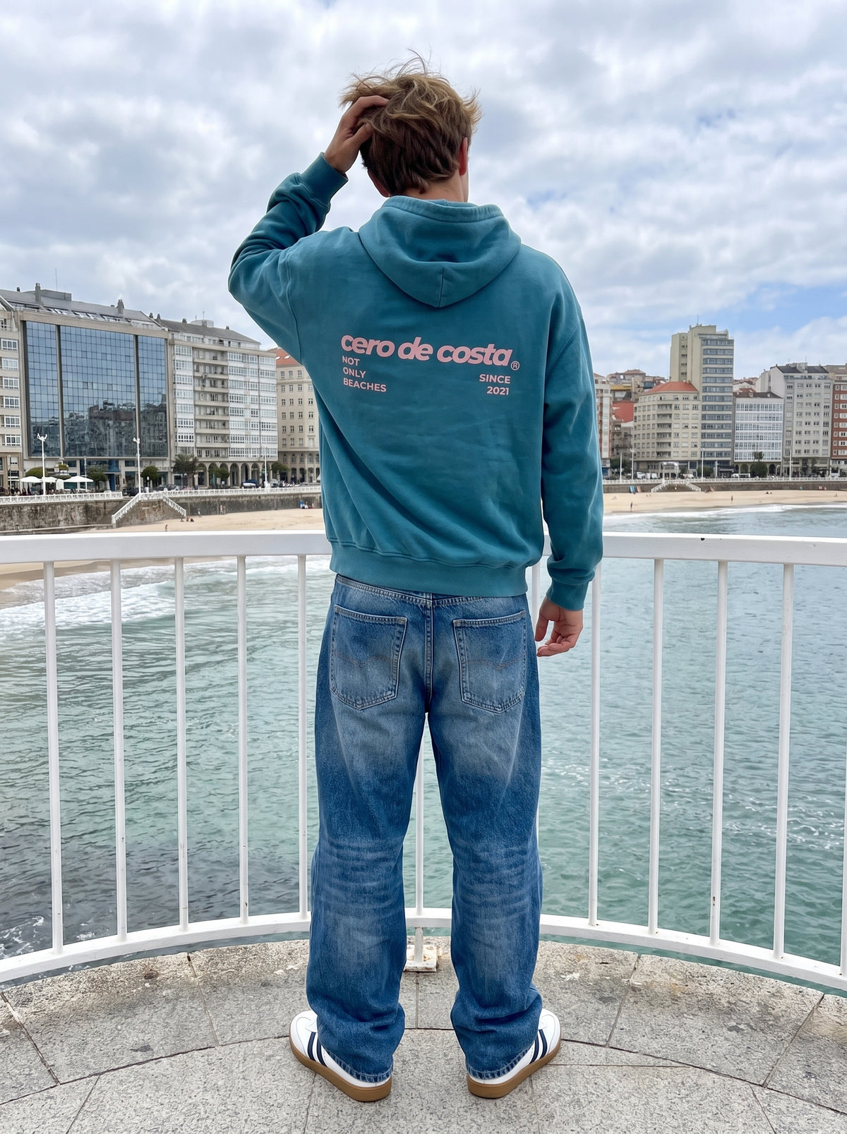 Espalda de la sudadera con capucha azul «Not Only Beach» frente a la playa del Orzán, A Coruña