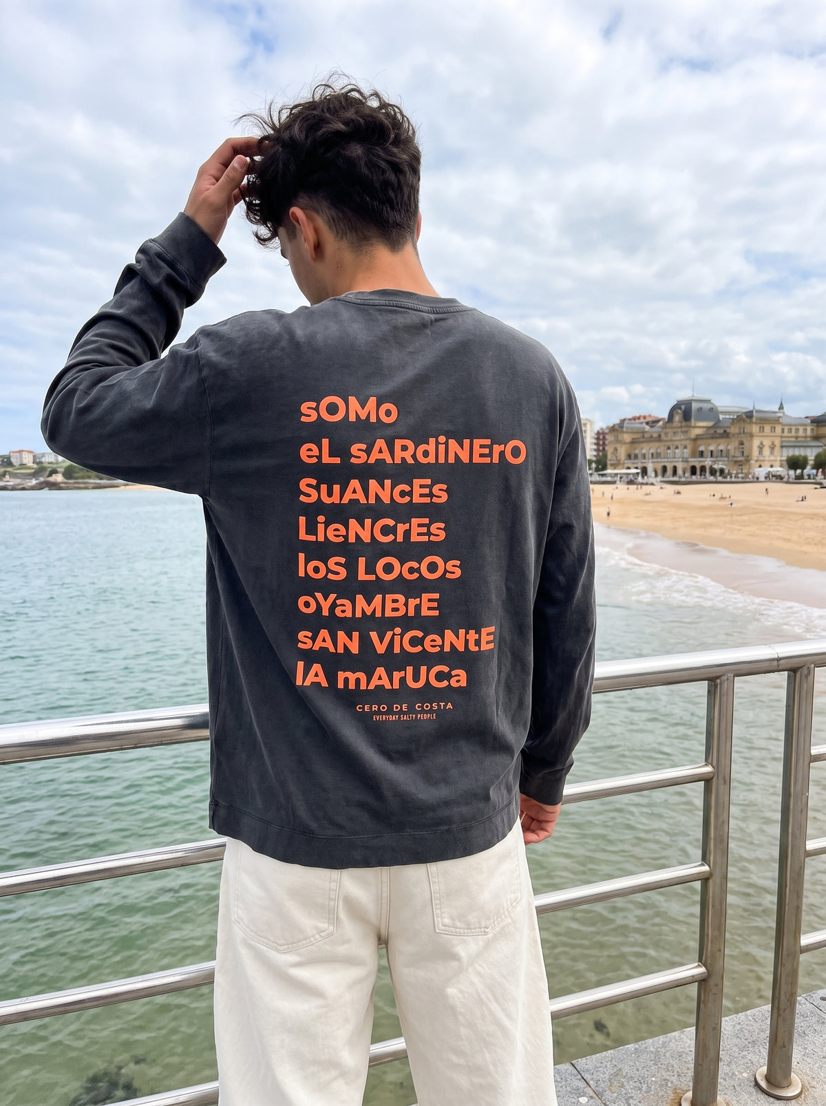 Espalda de la camiseta antracita «Cantabria» con la lista de playas cántabras en naranja, en El Sardinero