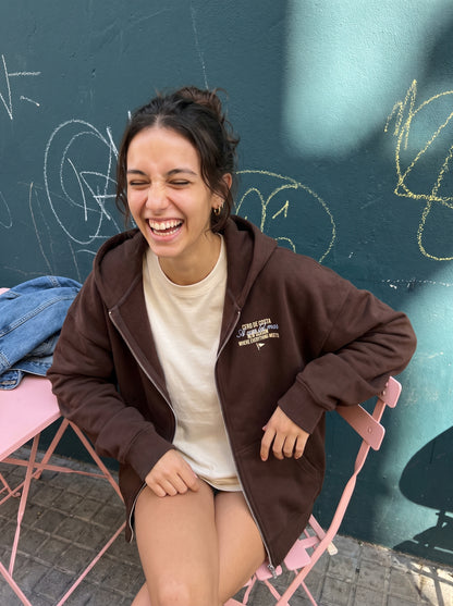 Sudadera marrón «Playas Surf» en una silla rosa de terraza